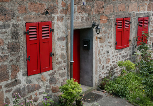 Ausschnitt einer Fassade eines alten aus Steinen gebauten Wohnhauses mit roter Tür und Fenstern mit roten Fensterläden