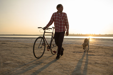 male bicycle rider walking on the sand, sunrise and lake or river background  