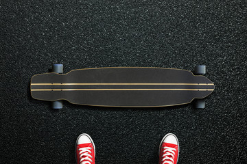 Long skateboard with sneakers on the asphalt road