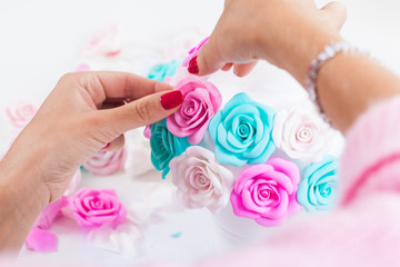Obraz na płótnie Canvas Close-up Young woman making her own hands artificial flowers roses from foam blue, pink white on a light table for decorating weddings and gifts