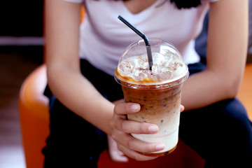Woman holding a plastic glass of iced coffee in coffee shop.