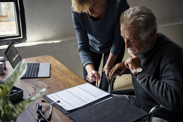 Side view of elderly man sitting on wheelchair looking at life insurance contract form