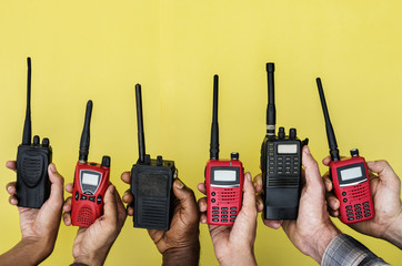 Group of hands holding portable two way radios with yellow background
