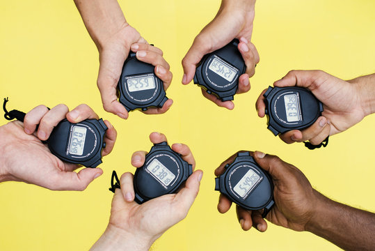 Closeup of hands holding stop watches with yellow background