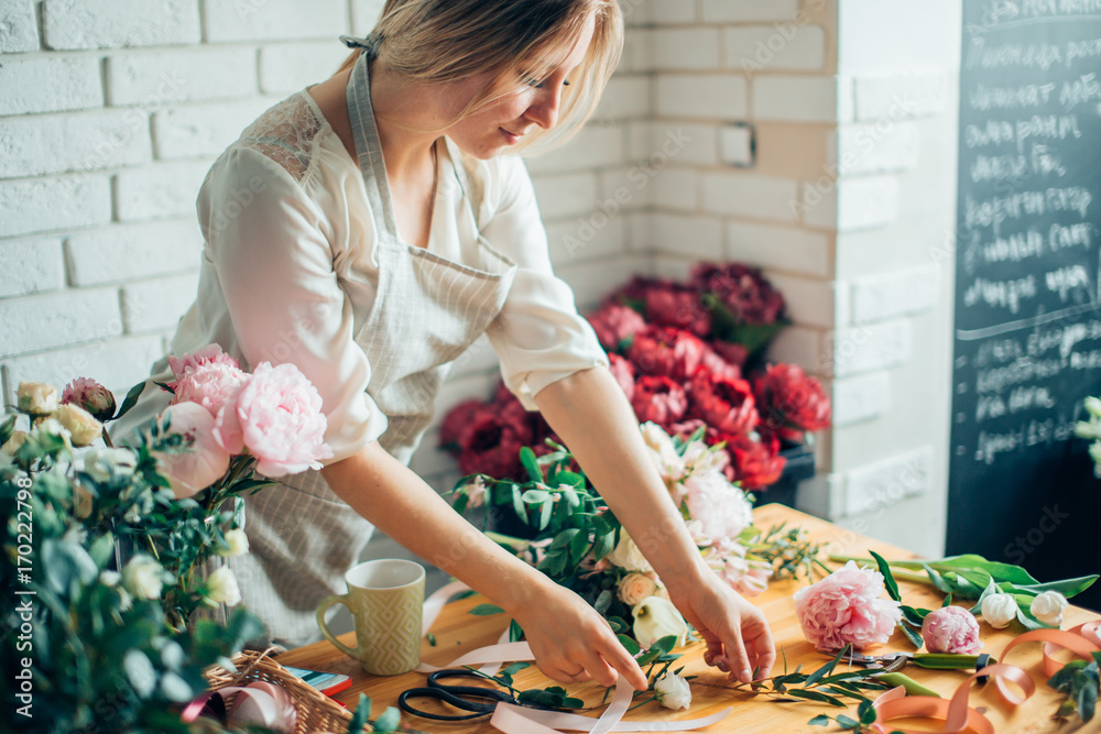 Wall mural Florist at work: pretty young blond woman making fashion modern bouquet of different flowers