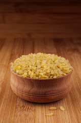 Bulgur in wooden bowl on brown bamboo board, close up. Rustic style, healthy dietary groats  background.