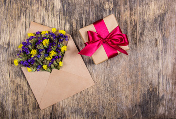 Wild flowers in an envelope and a gift box with a bow on an old wooden background. Romantic concept.