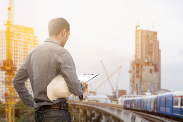 civil engineer holding helmet and working checklist construction with building construction and crane construction background