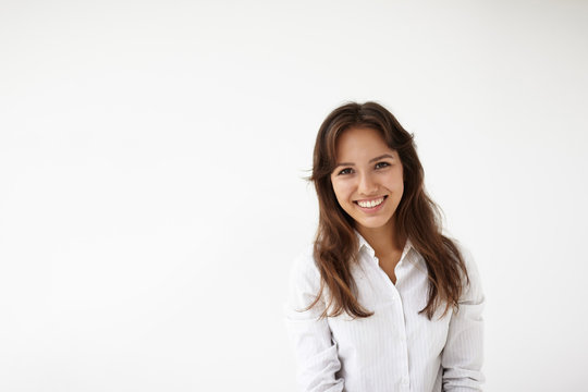 Isolated picture of natural positive young woman employee of mixed race appearance dressed in white blouse, looking at camera with pleased joyful smile, happy after she got promotion at work