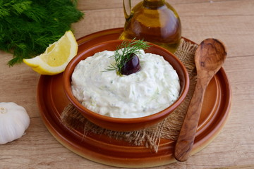Tzatziki - yoghurt sauce with cucumber, dill, olive oil, lemon and garlic in a traditional bowl,traditional greek cuisine.Twooden background. op view