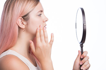 Unhappy young pretty girl looking at her pimple on her face in the mirror
