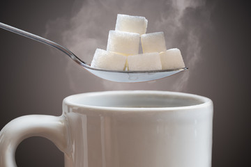 Unhealthy eating concept. Many sugar cubes above hot cup of tea or coffee.
