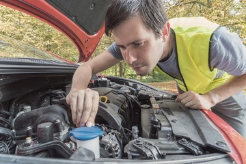 Man is repairing car and checking engine coolant.
