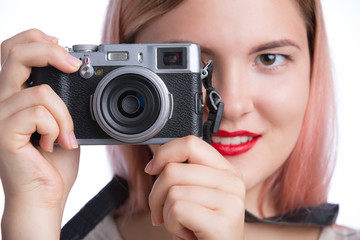 Young stylish girl taking photo with retro camera and looking at camera on white background