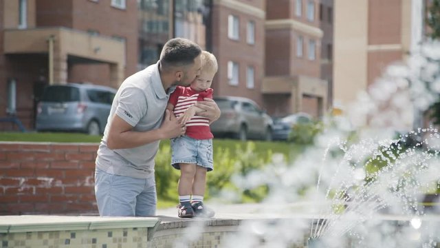 A little boy walks with his father and happily runs along the fountain, holding his hand. A little boy is happy, looking at the fountain, the father keeps him