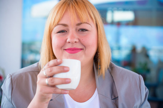 A woman of size plus a US or European saithe sitting in a restaurant drinks coffee in a good mood. A young girl with excess weight, stylishly dressed in the center of the city is waiting for a friend