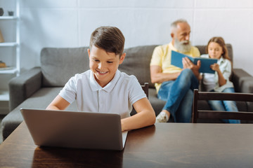 Fototapeta premium Boy playing on laptop while sister and grandfather reading book
