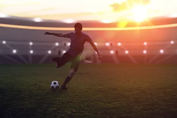 Fototapeten Soccer player is kicking a ball to the net in stadium at sunset. © vchalup