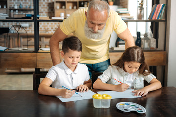 Loving grandfather watching grandchildren paint watercolor pictures