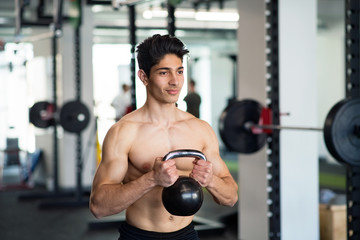 Young fit hispanic man in gym exercising with kettlebell.