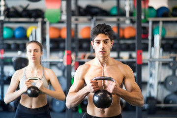 Fototapeta premium Young fit couple in gym exercising with kettlebell.