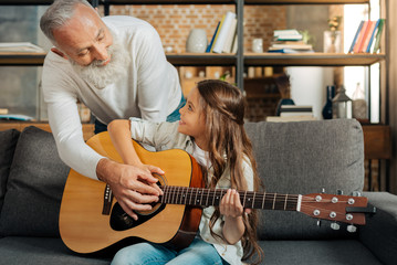 Loving grandfather teaching his granddaughter how to play guitar