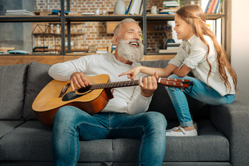 Grandfather chatting with granddaughter while holding guitar