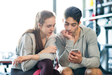 Fit couple in modern crossfit gym with smartphone.