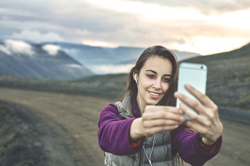 Girl in warm clothing makes selfie photo on background of mountains and sea of Iceland. women on the road thru a mountain pass, fjord is on background