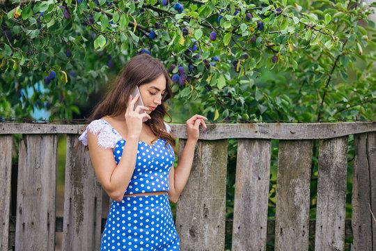 Woman talking on smart phone outdoors. Cropped image of young pretty trendy girl  posing at the country on old fence background using mobile phone.