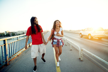 Young hipster couple walking on the bridge at sunset.