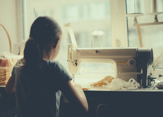 Little girl working on sewing machine at home.