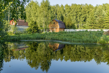 Obraz premium Wooden gottage near old pond and forest with reflection in water
