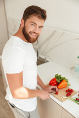 Vertical image of smiling bearded man cuts vegetables on kitchen