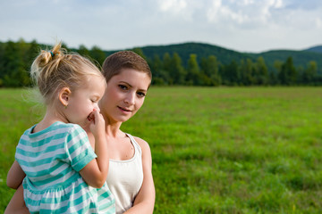 Attractive young mother carrying preschool daughter in her arms during a walk through a meadow