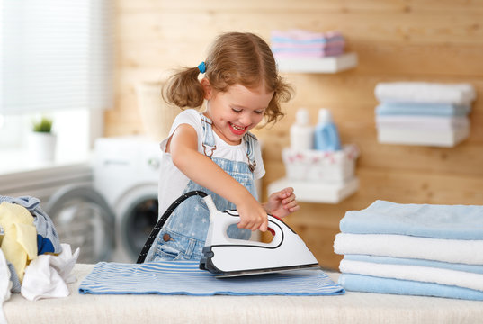 Happy   child girl ironing clothes   in laundry