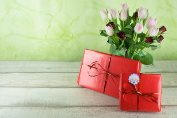 Zwei rot verpackte Geschenke mit Schleife auf einem Holztisch mit einem Strauß Blumen, Rosen und...