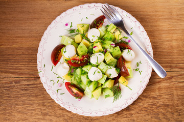 Avocado salad with tomato, cucumber and mozzarella. Cheese and vegetable salad. View from above, top studio shot
