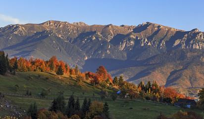 Autumn landscape in mountains. Deciduous forest in hills. Stack dry hay in meadow. Beautiful sunset.