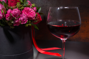 Glass with wine standing by bouquet of roses