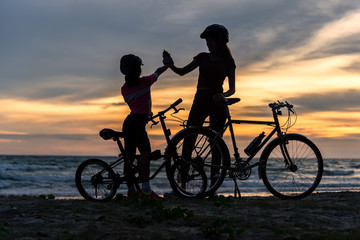 Obraz premium Biker family silhouette at the beach at sunset..