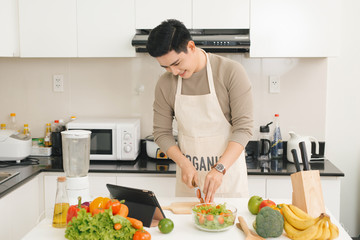 Asian handsome man looking recipe on laptop in kitchen at home