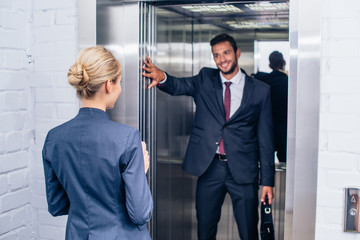 Businessman holding elevator door for woman