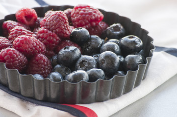 Blueberries and Raspberries in the black vintage metal bowl on a rustic wooden board