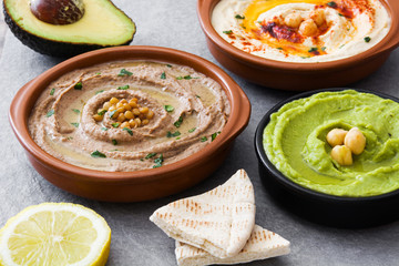 Different hummus bowls. Chickpea hummus, avocado hummus and lentils hummus on gray stone
