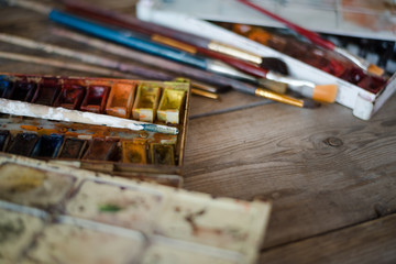 Background with used paint brushes and watercolor paints on old wooden boards. Place for text. Top view with copy space