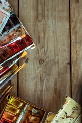 Background with used paint brushes and watercolor paints on old wooden boards. Place for text. Top view with copy space