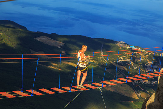 Woman is walking along a suspension bridge over an abyss.