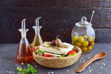 Traditional greek salad with cucumber, onion, tomato, paptika, feta cheese, olive oil and oregano in a eatable bowl made of a special traditional rye dough with glass jars with olive oil , vinegar and