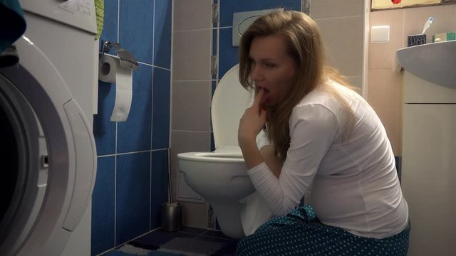 attractive lovely pregnant woman kneeling down and vomiting into toilet